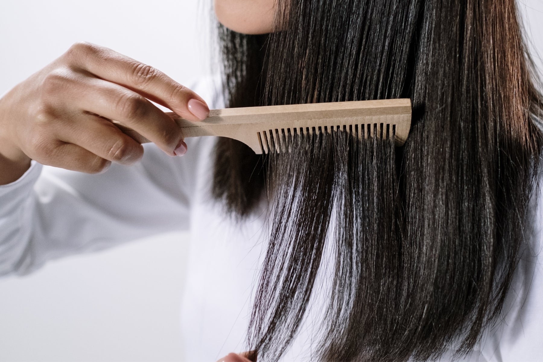 Mujer peinando su cabello con un peine de madera, mostrando un cabello largo y saludable.