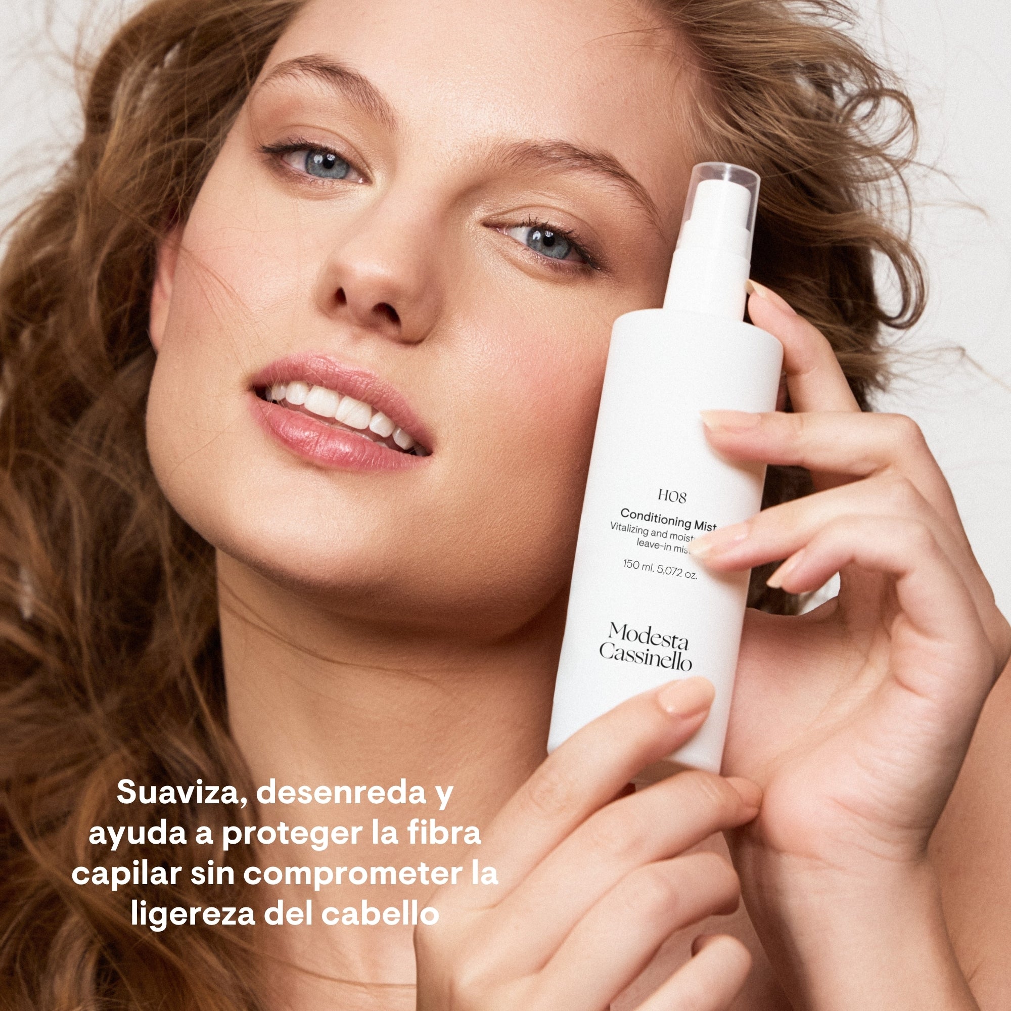 Chica con cabello ondulado sosteniendo la bruma acondicionadora H08 de Modesta Cassinello, suaviza, desenreda y protege la fibra capilar sin comprometer la ligereza del cabello